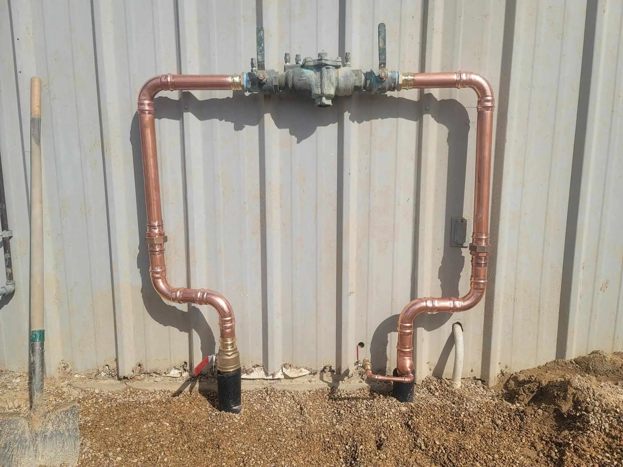 Backflow assembly with copper piping mounted on a metal building wall