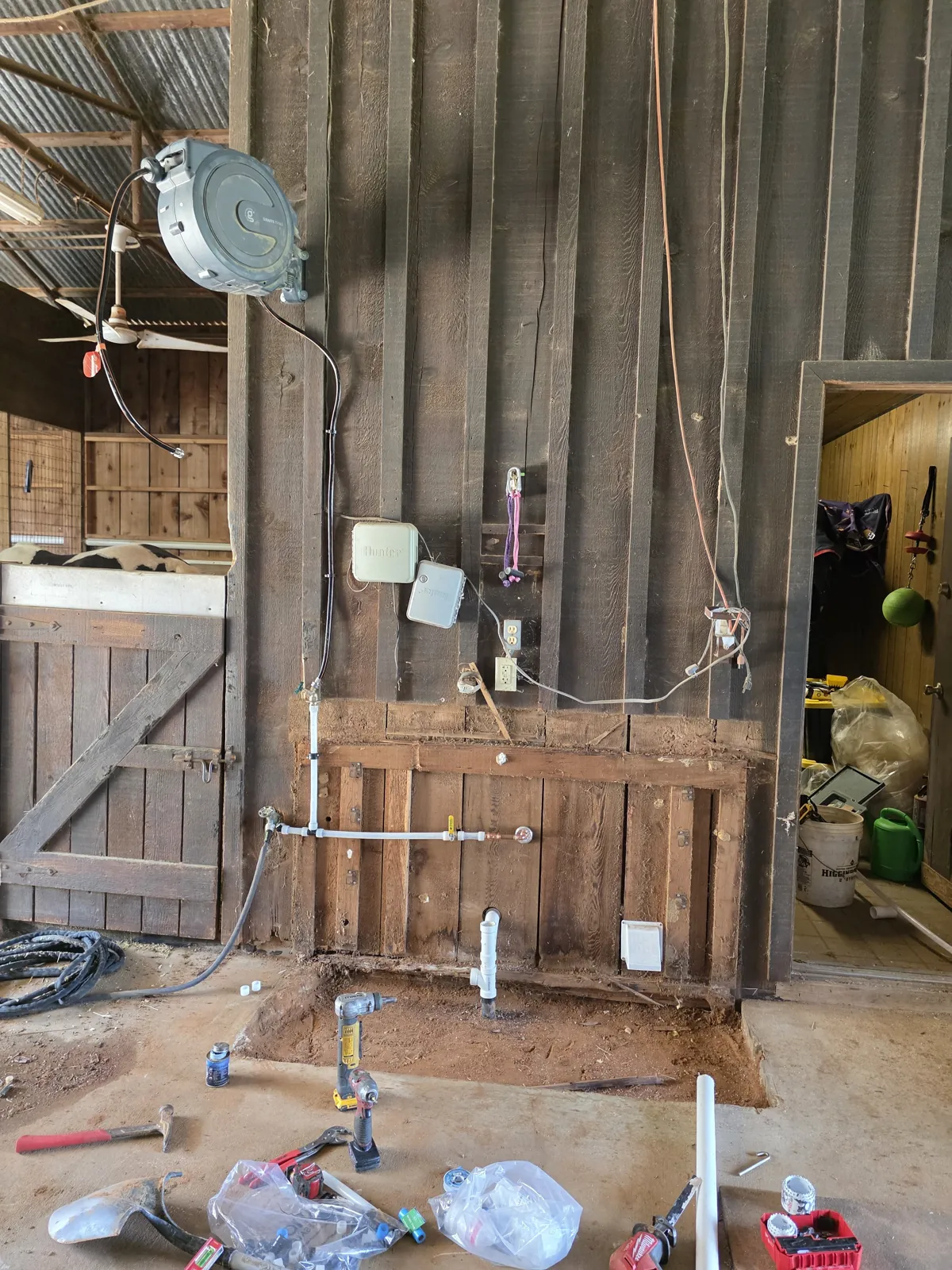 Barn wall with new supply lines and a drain stub over a cut slab, tools on the floor