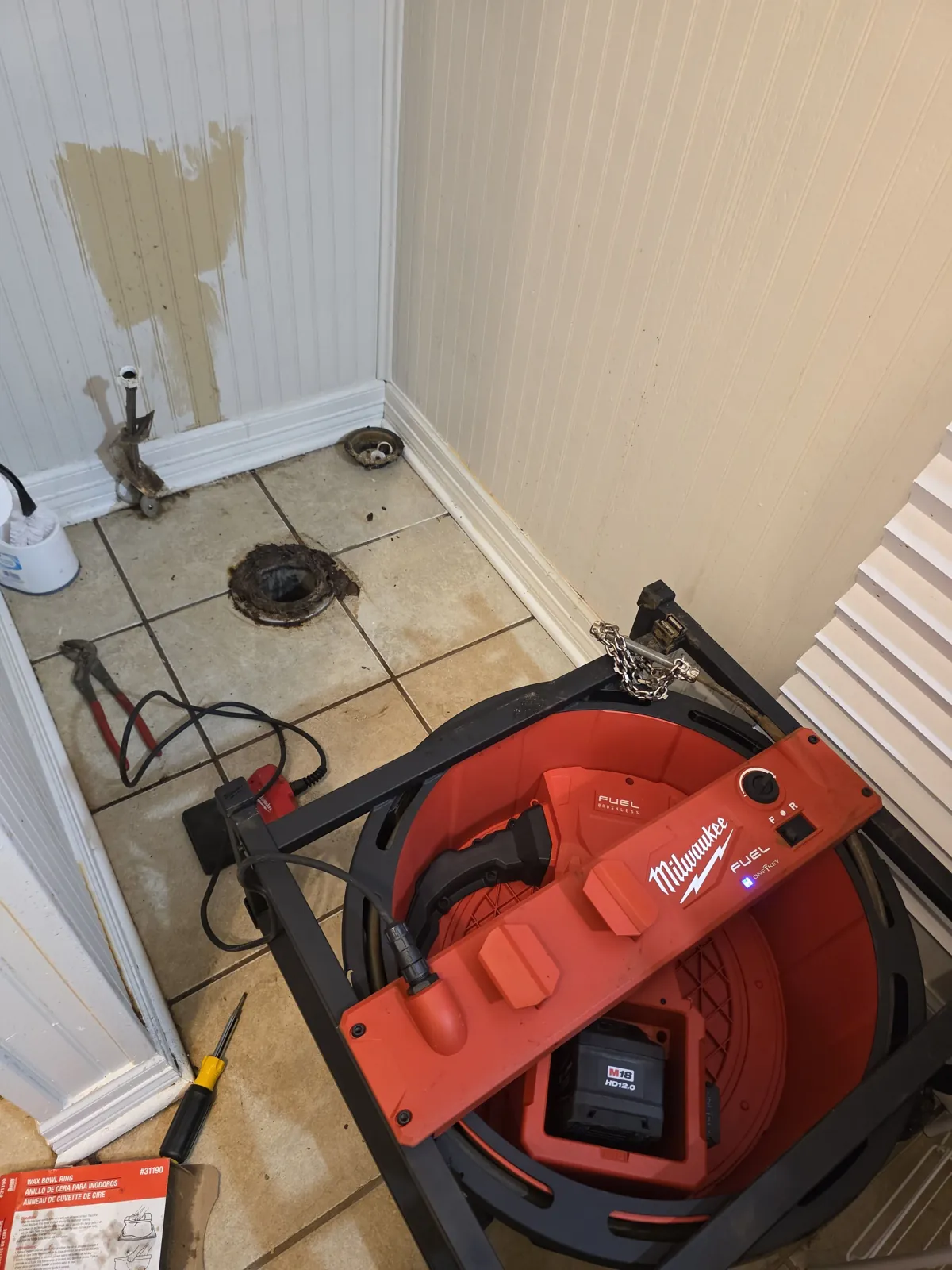 Drain cleaning machine set up in a bathroom with the toilet pulled
