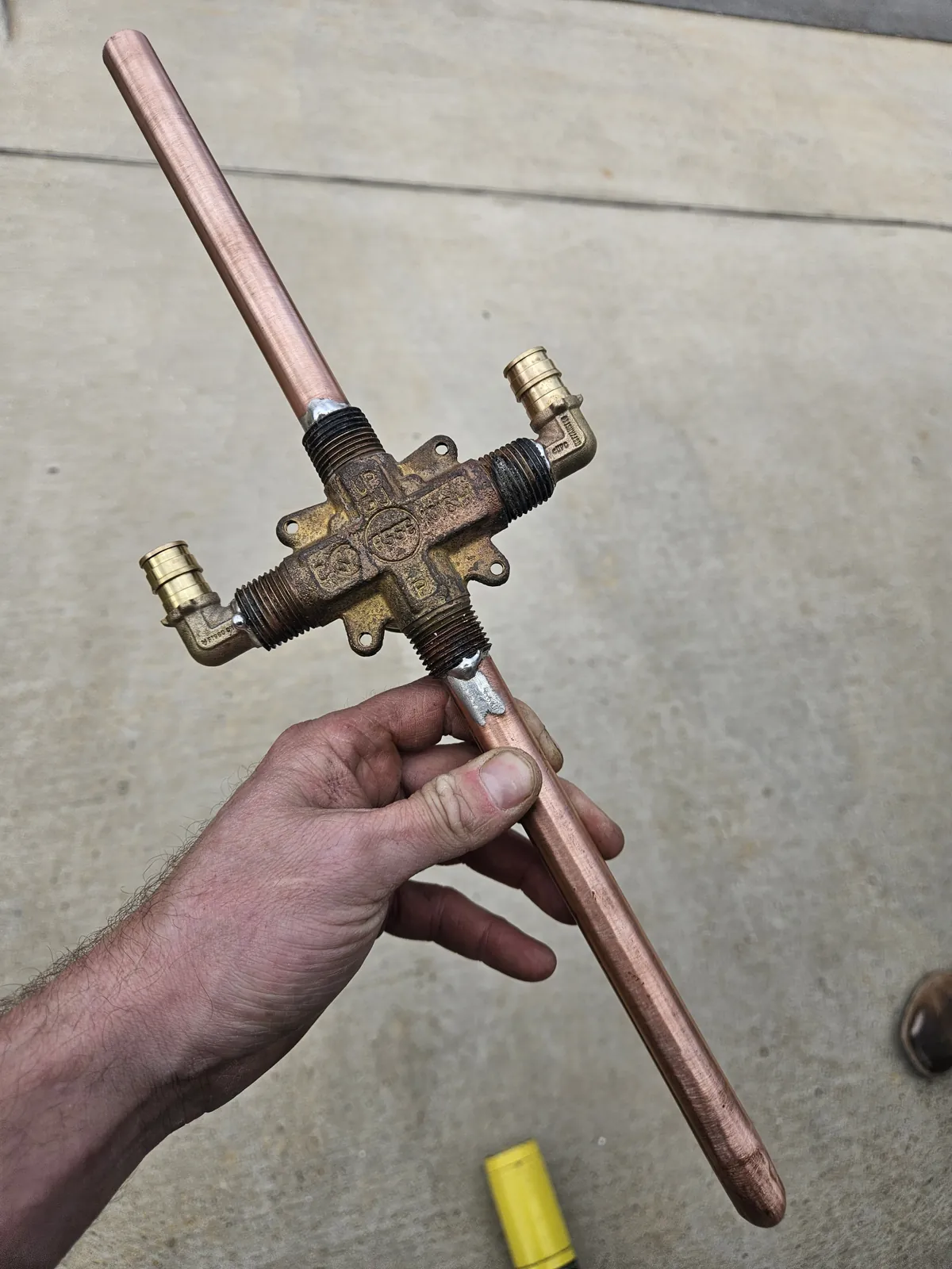 Brass shower valve body with a copper riser held above a concrete driveway