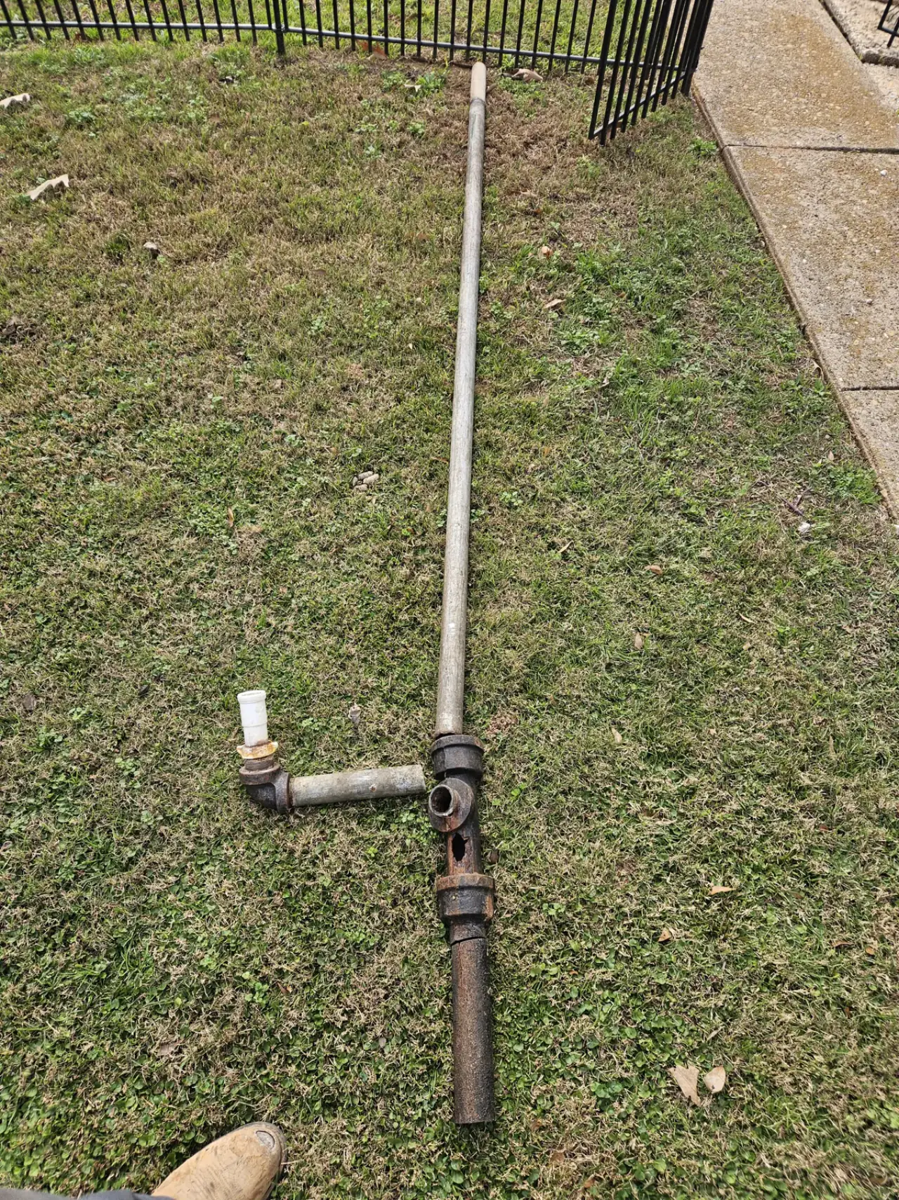 A long run of old galvanized pipe with rusted cast fittings pulled out and laid on a lawn beside a sidewalk, in East Texas