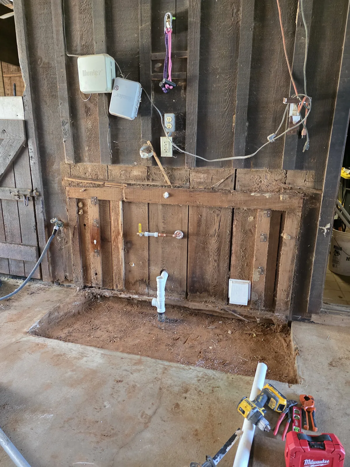 Barn wall with supply piping and a PVC drain stub above a cut section of slab