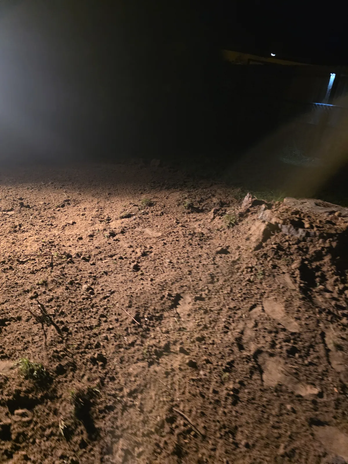 Graded dirt over a filled trench, lit by a work light at night